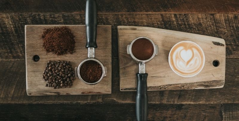 Fresh coffee grounds on a wooden board next to a cup of coffee.