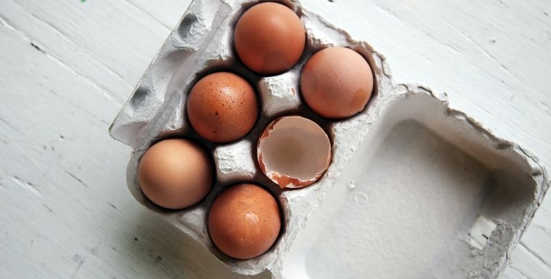 Eggs and eggshells in a cardboard carton.