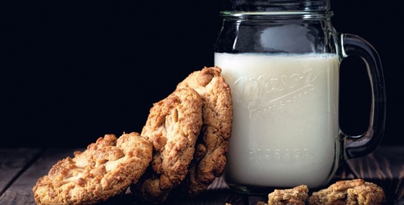 A cup of milk supports three freshly baked cookies.