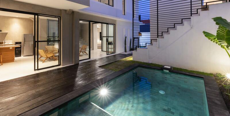 In ground swimming pool in an outdoor area of a modern home. There is wooden decking, plants and outdoor lighting. 