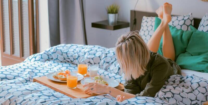 Blonde woman relaxing on bed with a breakfast beside her.